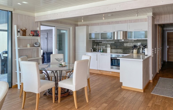 Une cuisine moderne avec des meubles blancs, un îlot central et un coin repas comprenant une table et des chaises en verre.