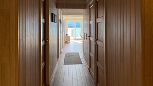 Un couloir en bois, avec un tapis menant à une porte donnant sur la mer.