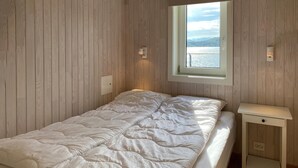 Une chambre à coucher avec un lit, une table de chevet, une fenêtre donnant sur un lac et des murs en bois.