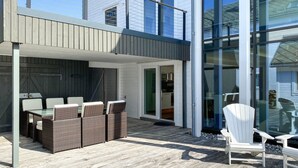 Une terrasse extérieure moderne, dotée de meubles en osier et d’une porte vitrée donnant sur la cuisine.