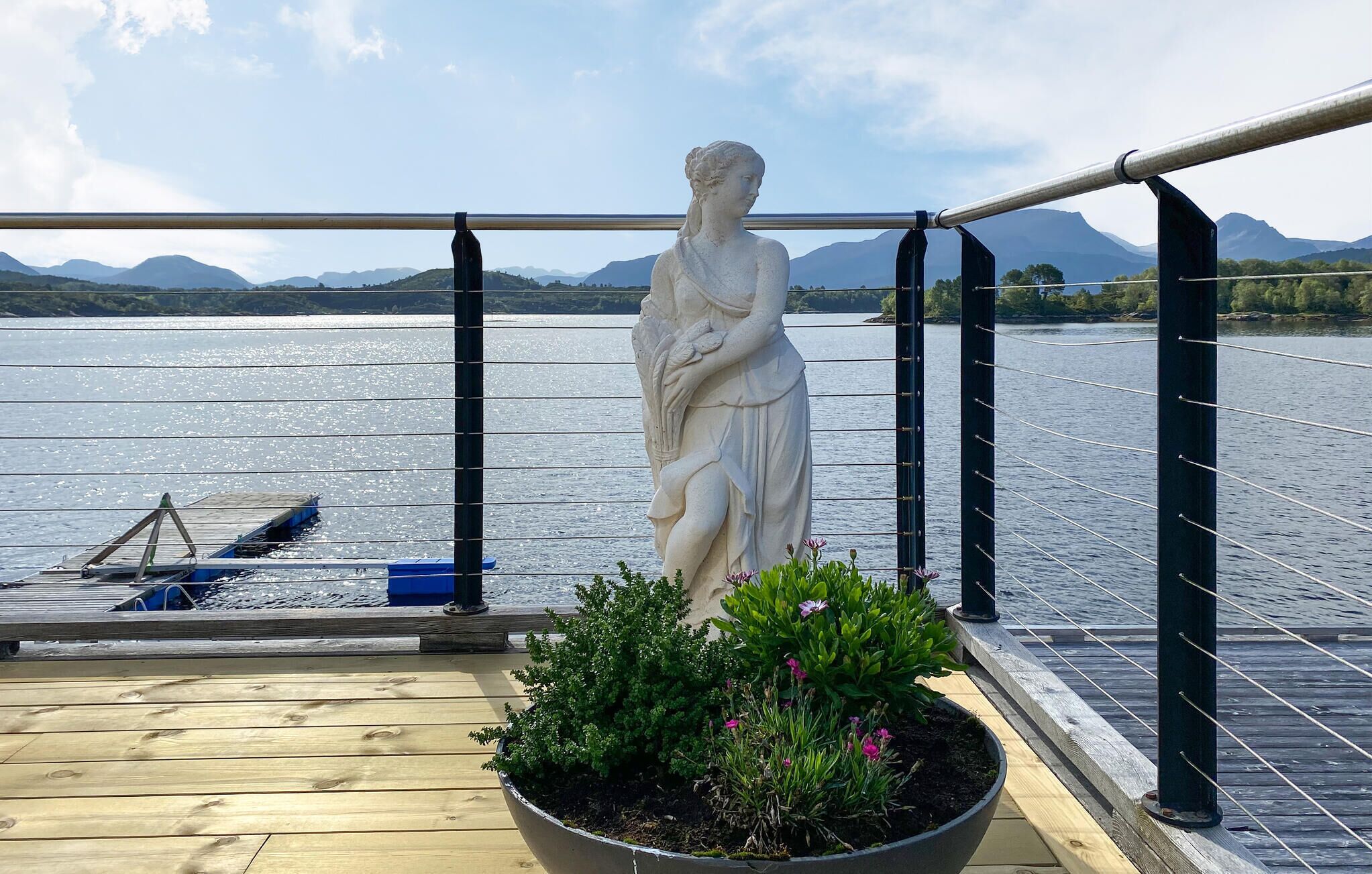 Eine Statue auf einem Deck mit Blick auf einen See und Berge.