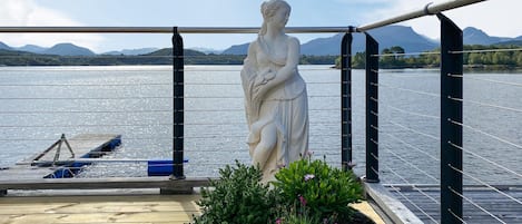 A statue on a deck with a view of a lake and mountains.