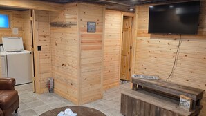 Een knus ingerichte kamer met houten details, een flatscreen televisie aan de muur, een houten bankje en een ronde salontafel.