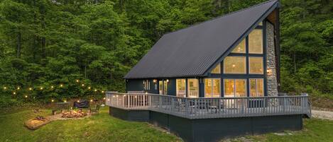 A cabin with a large deck, surrounded by dense forest.