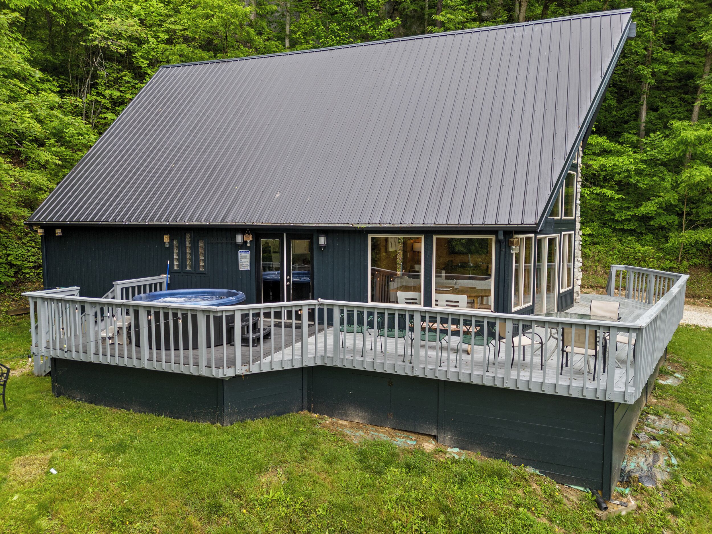 A two-story cabin with a deck, a hot tub, and a covered outdoor seating area.