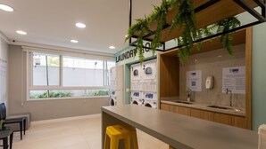 A laundry area with washing machines, a sink, and a table with a stool. - Studio With Balcony 500m From the Metro - Mop0103 (São Paulo)