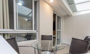 Ein Glastisch mit vier Korbstühlen, ein Fenster mit Jalousien und eine Deckenleuchte.