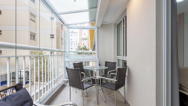 A balcony with a glass door, a round table, and four wicker chairs. - Studio With Balcony 500m From the Metro - Mop0103 (São Paulo)
