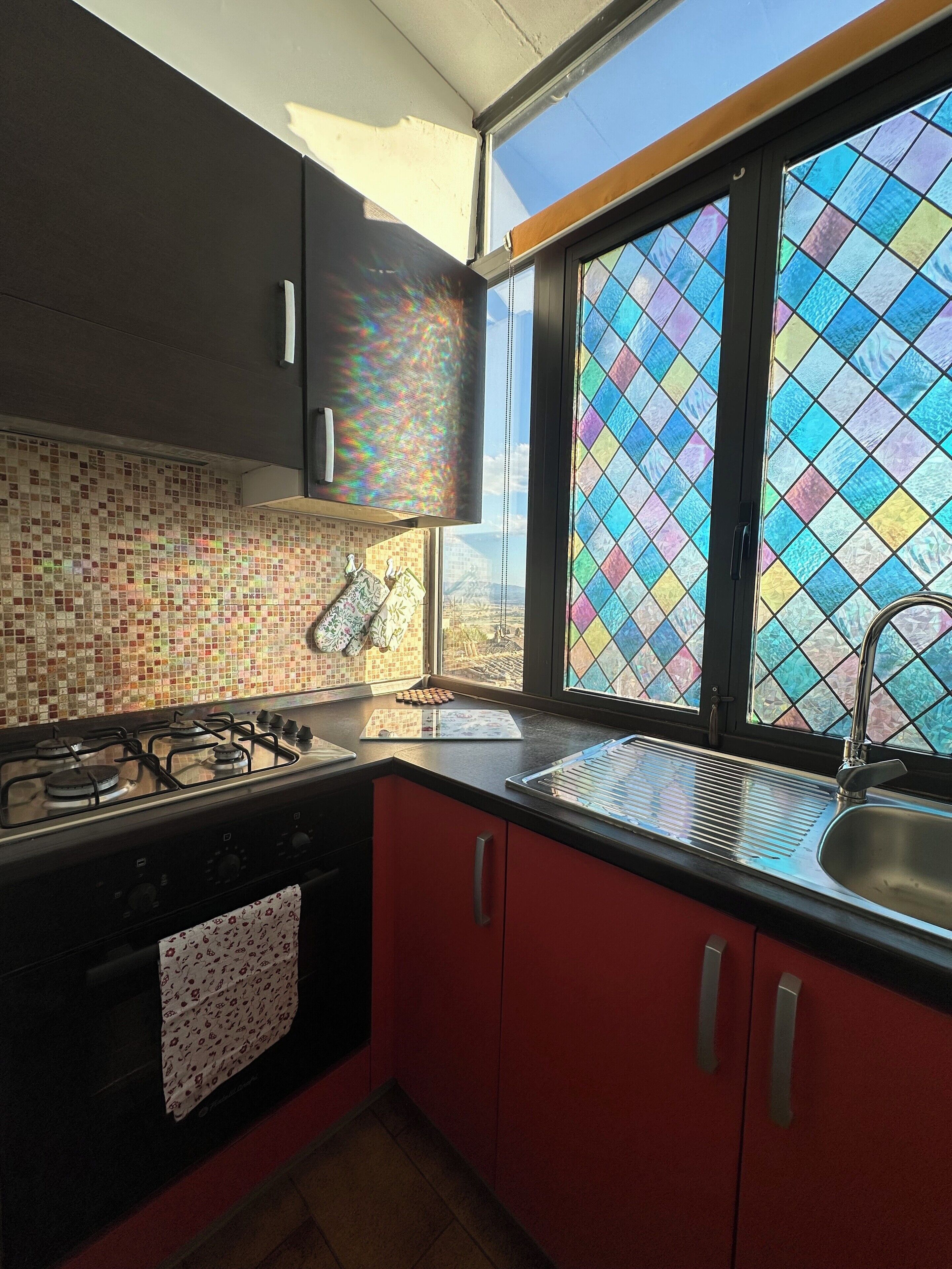 A kitchen with a gas stove, a sink, and a window with colorful stained glass.