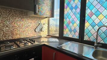 A kitchen with a gas stove, a sink, and a window with colorful stained glass.