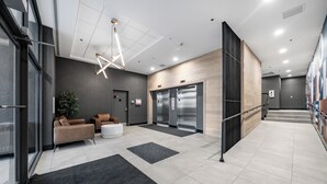 A modern lobby with a sofa, a plant, a staircase, and elevators. - Stylish Condo W/ Stunning views & Short Walk DT (Calgary)