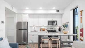 A modern kitchen with white cabinets, stainless steel appliances, and a central island with stools. - Stylish Condo W/ Stunning views & Short Walk DT (Calgary)