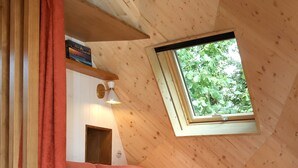 Une pièce chaleureuse avec un plafond en pente, un canapé rose, une petite table ronde et une fenêtre donnant sur un paysage verdoyant.