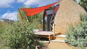 Une structure en forme de dôme géodésique, dotée d’une terrasse en bois et d’une toiture rouge.