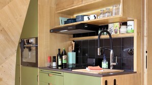 Une cuisine compacte avec des meubles verts, un plan de travail noir et un four encastré.