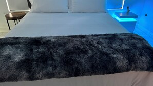 A modern bedroom with a large bed, a fluffy dark throw blanket, and a bedside table with a remote control. - Ocean View Apartment with AC – Steps to Doctor’s Cave Beach (Montego Bay)