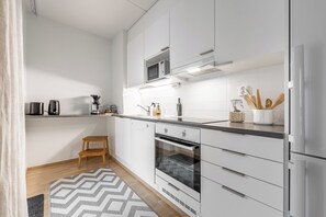 A modern kitchen with white cabinetry, a microwave, an oven, and a small wooden stool.