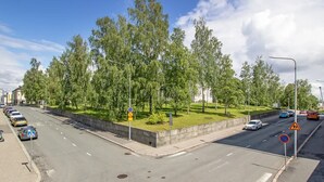 A road intersection with a grassy median, cars parked on the side, and a pedestrian crossing sign. - Stylish Nordic 2BR Apartment with Sauna (Kuopio)