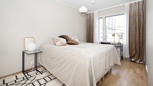 Un dormitorio con cama, una mesita de noche con lámpara, una ventana con cortinas y vistas al exterior.