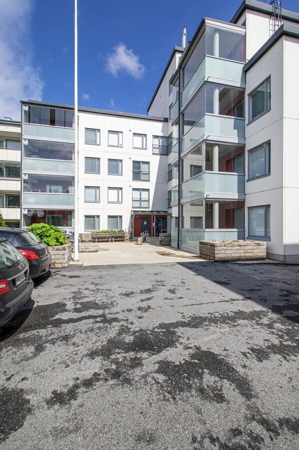 A modern apartment building with multiple balconies, a parking area, and a clear sky. - Stylish Nordic 2BR Apartment with Sauna (Kuopio)