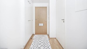 Un pasillo estrecho con una puerta de madera al final, paredes blancas y una alfombra estampada en el suelo.