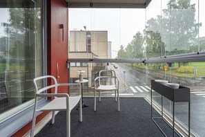 A sheltered seating area with tables and chairs, a glass barrier, and a view of the road and greenery outside. - Stylish Nordic 2BR Apartment with Sauna (Kuopio)