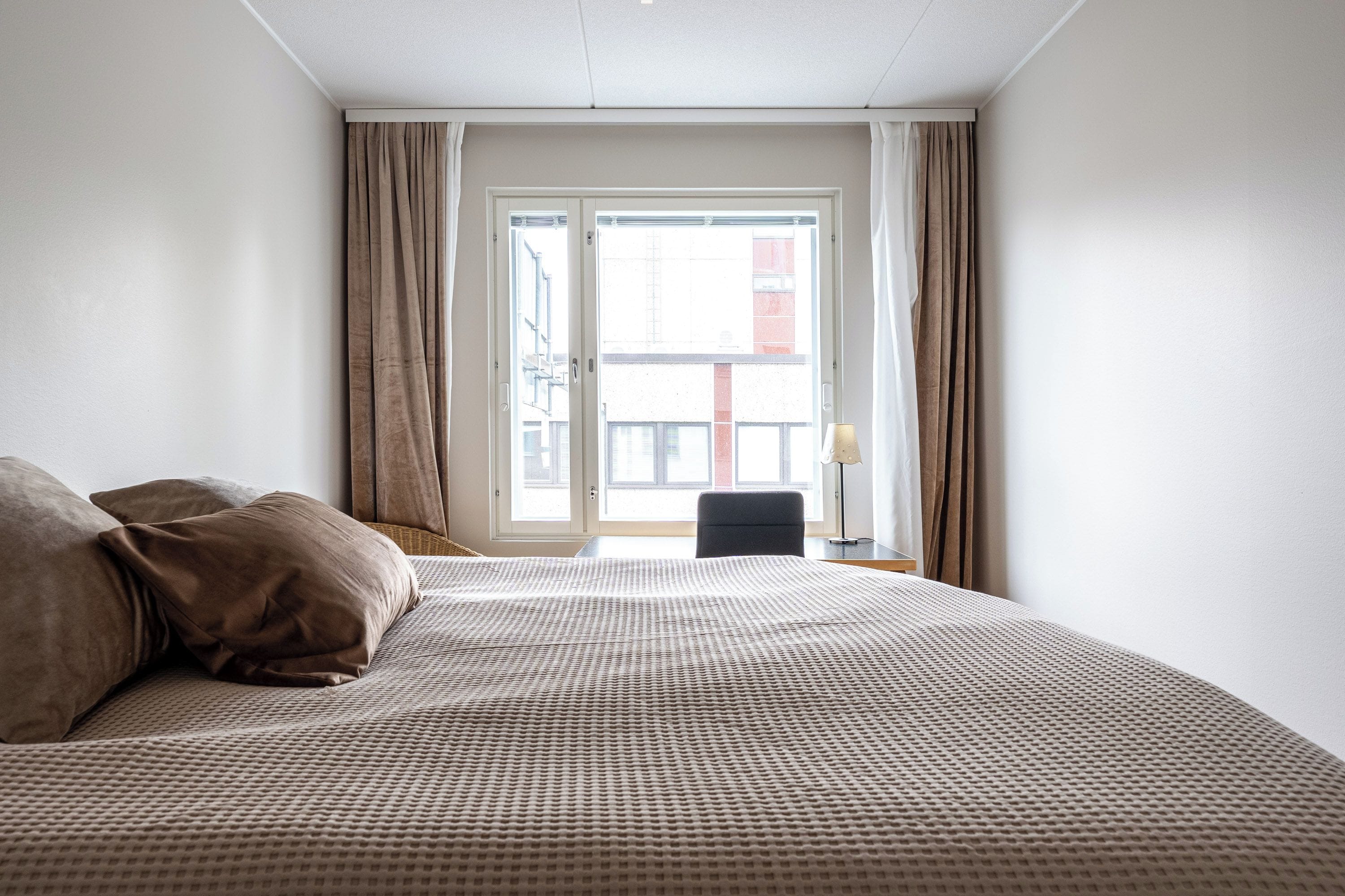A hotel room with a large bed, a chair, and a window with curtains.