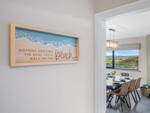 Un comedor con una mesa lista para cuatro personas, vistas al exterior y una obra de arte con temática playera.