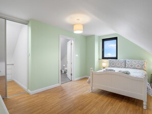 Een slaapkamer met een schuine kap, een bed met een gestreept hoofdeinde, een bedlampje en een raam met uitzicht.