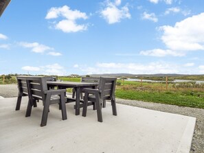 An outdoor seating area with a table and chairs, a concrete floor, and a view of a lake and hills in the background.