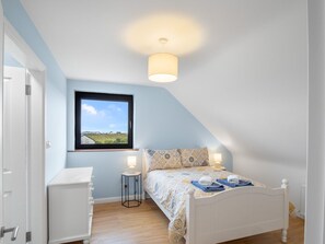 A bedroom with a bed, bedside tables, a window with a view, and a ceiling light fixture.