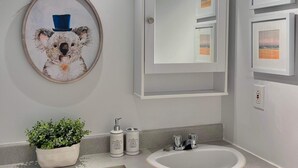 Bagno con WC, lavabo e specchio. Si nota un quadro con un koala appeso al muro, una pianta in vaso e un lampadario sopra lo specchio.