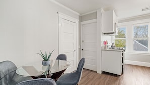 A modern kitchen with white cabinets, a glass table, and grey chairs.