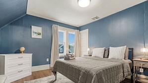 A bedroom with a bed, dresser, nightstand, and a window with curtains.