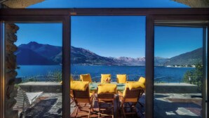 A terrace with a table and chairs, overlooking a lake with mountains in the background.