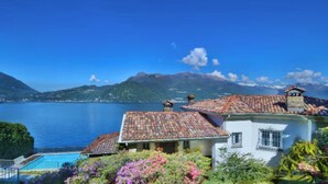 A coastal villa with a swimming pool, terraced roofs, and a view of the sea and mountains.