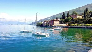 A calm lake with several boats anchored near a hillside with buildings.