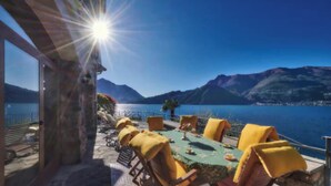A terrace with a table and chairs, overlooking a body of water and mountains.