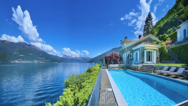 A swimming pool with a mountain view, a house with a balcony, and a clear sky.