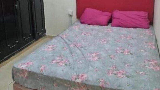 Une petite pièce avec un lit, une tête de lit rouge et une armoire.