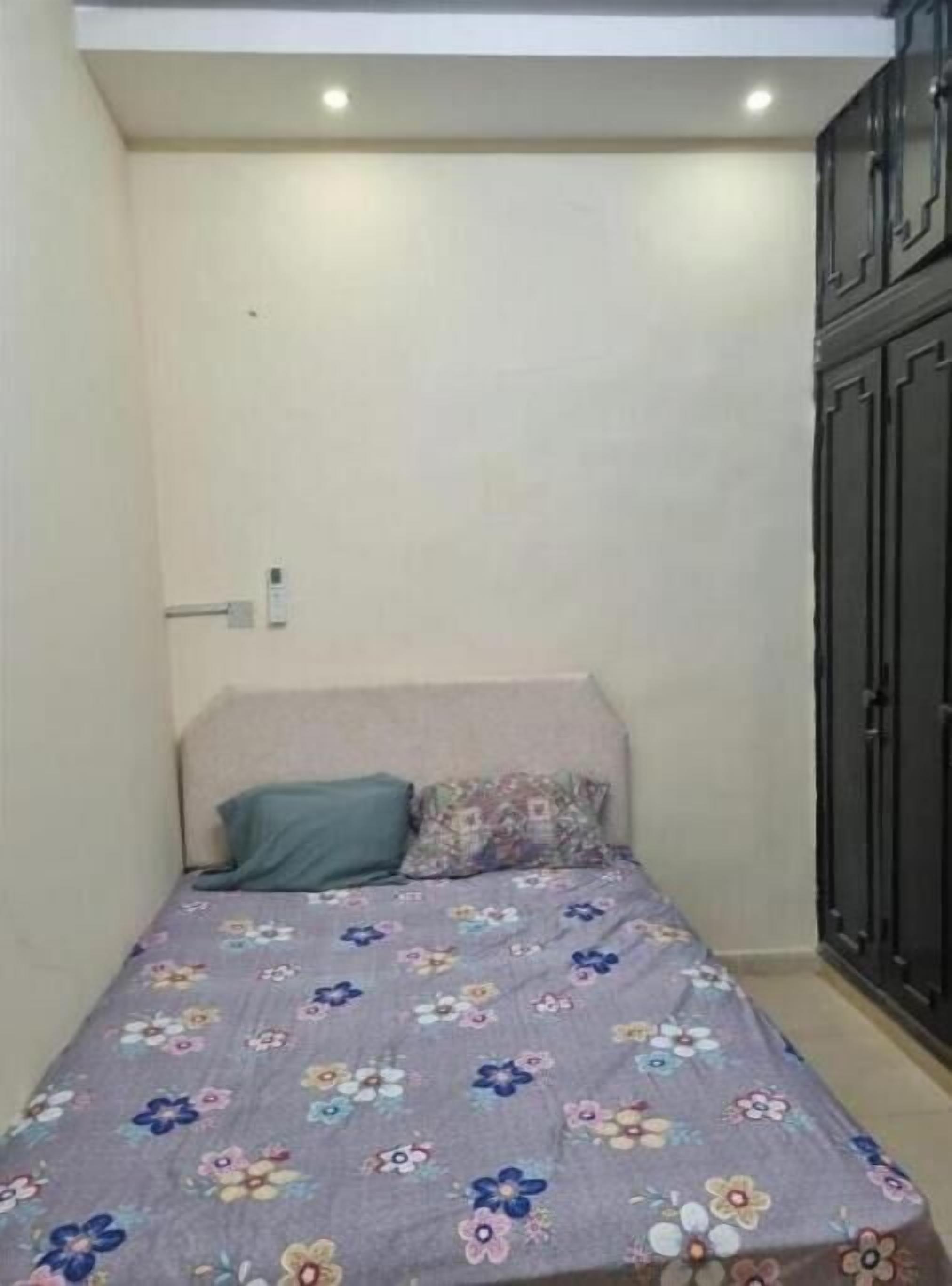 Una habitación pequeña y estrecha con una cama individual cubierta con una colcha estampada de flores.