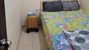 Ein kleines Zimmer mit einem Bett, einer Klimaanlage, einem kleinen Hocker und einem Bild an der Wand.