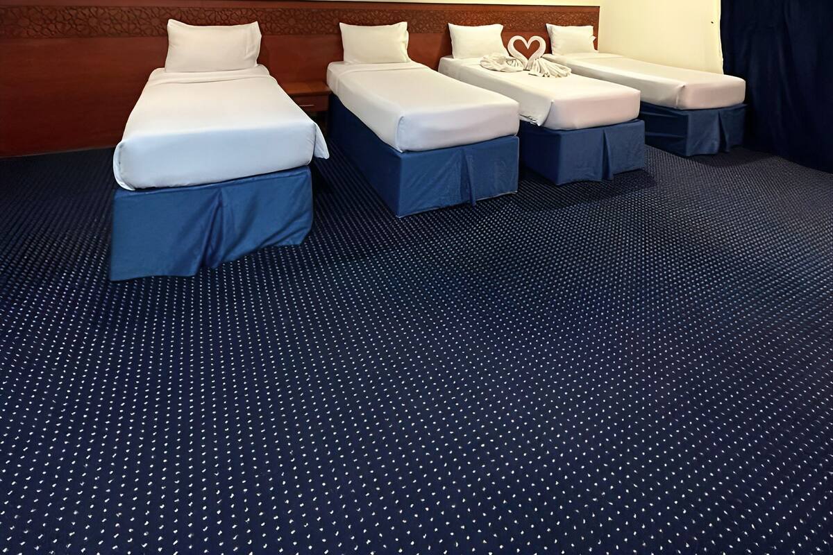 Een hotelkamer met drie bedden, een grote plafondlamp en een kamerbreed tapijt met patroon.