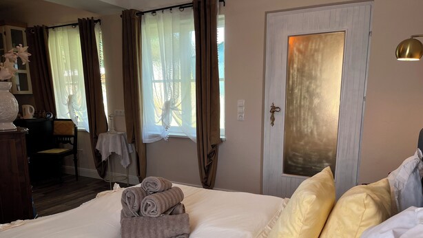 A neatly made bed with rolled towels, a bedside table, a chair, and a door with a mirror.