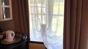A room with a window covered by sheer curtains, a white kettle on a tray, and a clock on the wall.