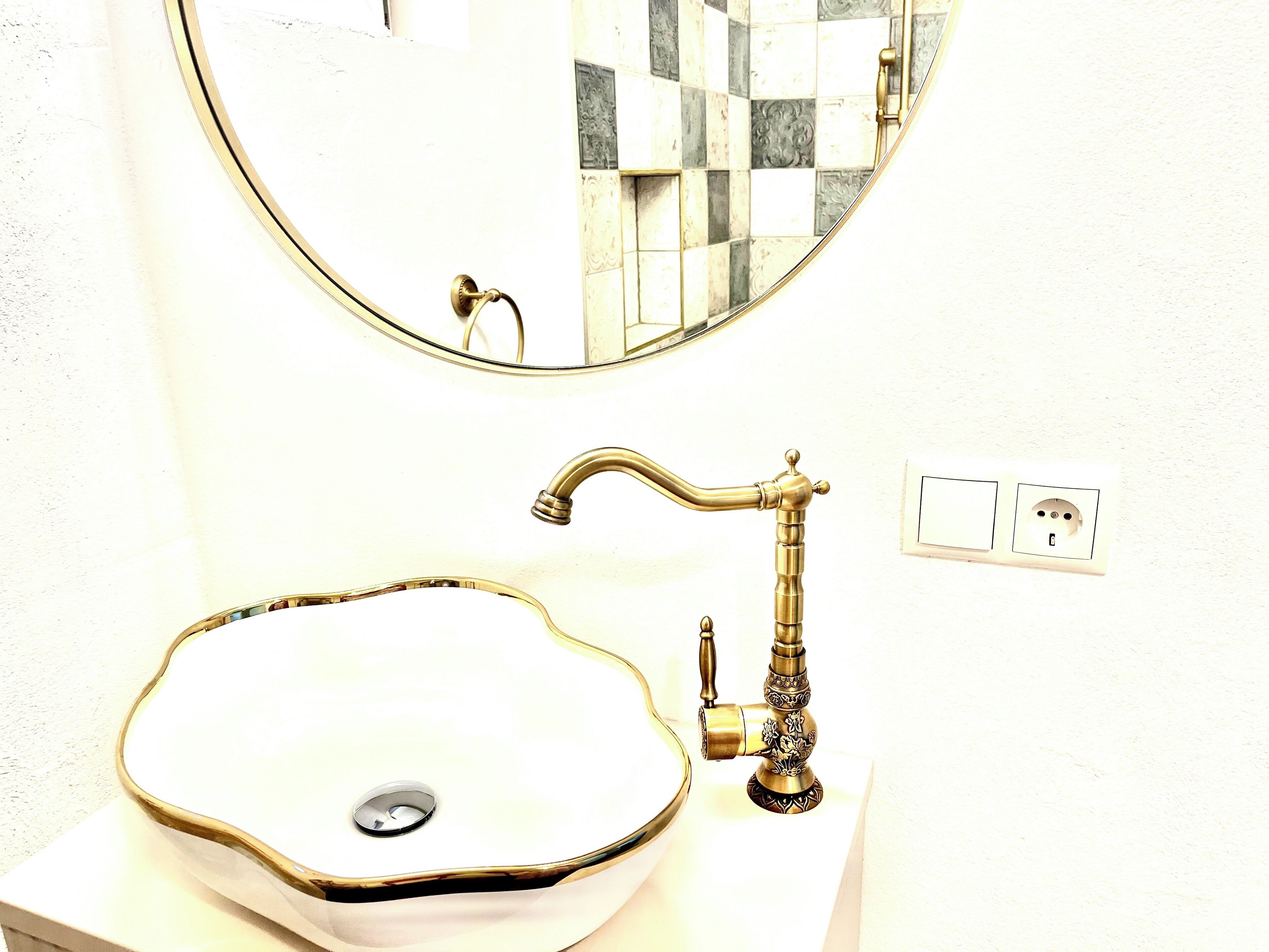 Une salle de bain avec un miroir rond, un lavabo blanc doté d’un receveur décoratif et un robinet en laiton.