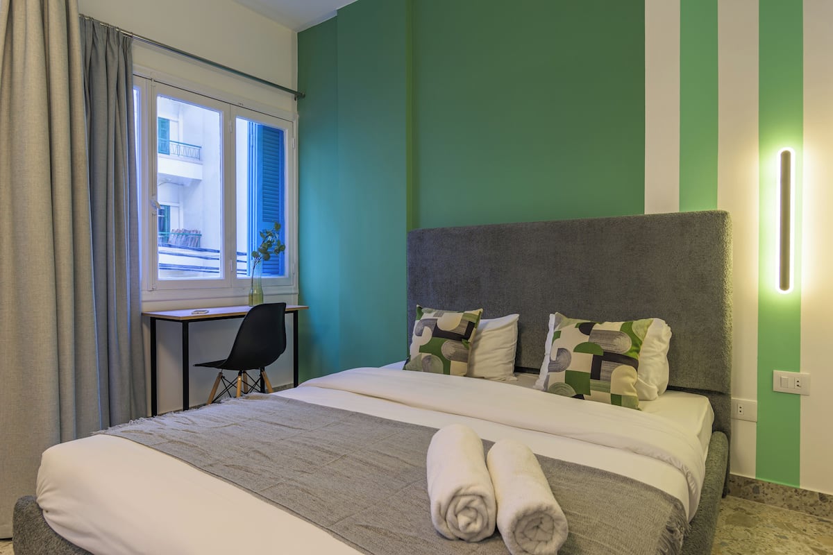 A hotel room with a bed, a desk, and a window with curtains.