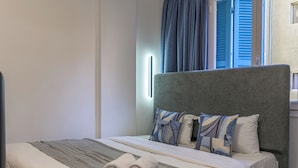Ein ordentlich bezogenes Bett mit grauem Kopfteil, zwei gerollten Handtüchern und einer grauen Decke.