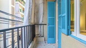 Ein schmaler Balkon mit Metallgeländer, einer blauen Rolltür und Blick auf ein Gebäude mit Balkonen und Geländern.
