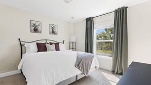 A bedroom with a bed, a bedside table, a lamp, and a window with curtains. - Sleeps 6 - 12 min from Fort Jackson - EV Charger & Pet Friendly! (Elgin)